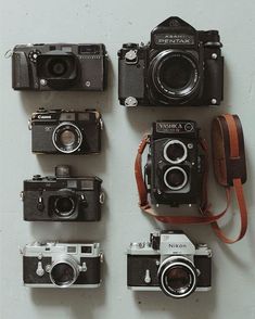 several different cameras sitting next to each other on a wall with leather straps around them