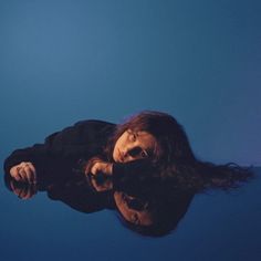 a woman with long hair standing in the water looking up at her reflection and smiling