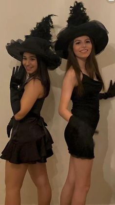 two women in black dresses and hats posing for the camera