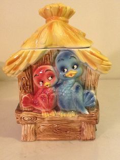 a ceramic figurine of two birds sitting under a yellow umbrella on top of a wooden structure