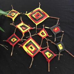 several pieces of art made out of sticks and colored paper on a black surface next to a plant