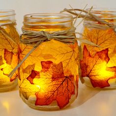 three mason jars filled with autumn leaves and twine tied to the lids, all lit up