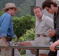 three men standing around talking to each other on a balcony with mountains in the background