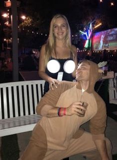 a man and woman in costumes are posing for a photo on a bench at night