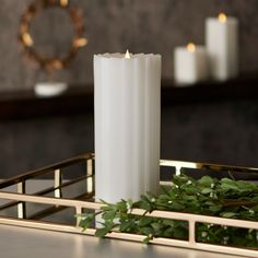 a white candle sitting on top of a metal tray next to candles and greenery