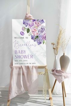 a welcome sign for a baby shower with purple flowers on it and a pink blanket