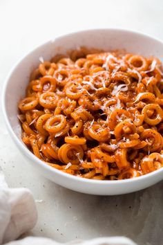 a bowl filled with pasta and sauce on top of a white tablecloth next to garlic