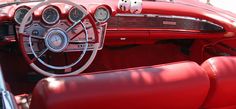 the interior of an old car with red leather seats and steering wheel covers on display