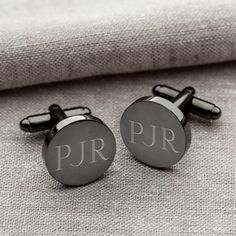 two cufflinks with the letters p r on them sitting next to a pillow