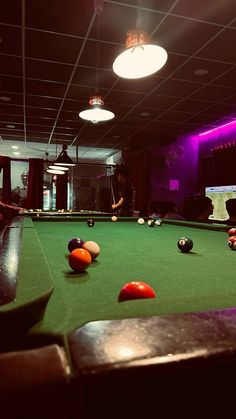 a pool table with several balls on it in a room that is lit up by purple lighting