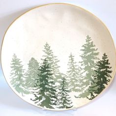 a green and white plate with trees painted on the side, in front of a white background