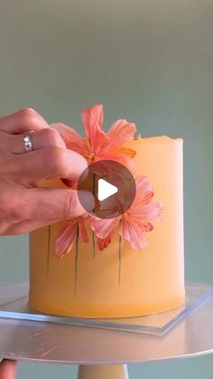 a person is decorating a yellow cake with pink flowers on the top and bottom