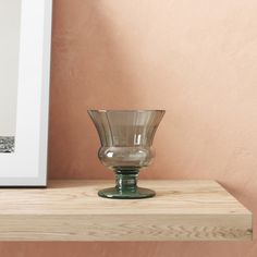 a glass vase sitting on top of a wooden shelf next to a framed photograph in a room