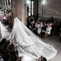 the bride is walking down the aisle with her veil in hand and people taking pictures