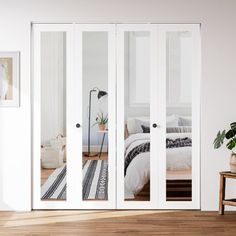 a bedroom with white walls and wooden flooring is seen through the sliding glass doors