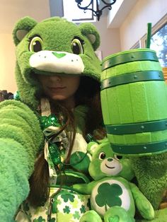 a woman in a green costume holding up a beer and two stuffed animals with shamrocks on them