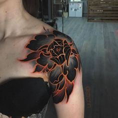 a woman's arm with a black and orange flower tattoo on her left shoulder