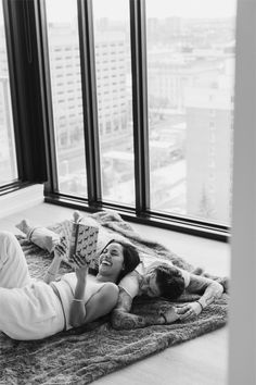 a woman laying on the floor with a book in her hand and another person holding a stuffed animal