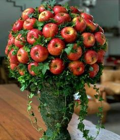 a vase filled with lots of red apples on top of a wooden table