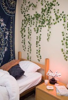 a bed with white sheets and pillows next to a wall hanging with vines on it