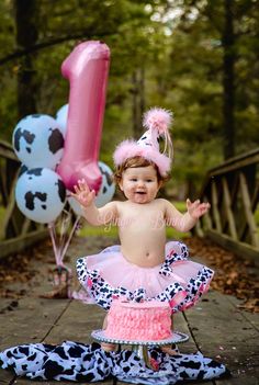 a baby girl wearing a cowgirl outfit and holding a number one balloon in her hand