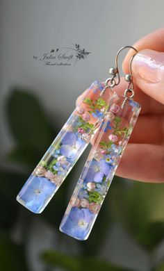 a pair of earrings with flowers and leaves on them are being held by a hand