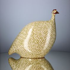 a ceramic bird sitting on top of a reflective surface in front of a gray wall