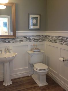 a white toilet sitting next to a sink in a bathroom under a mirror on top of a wooden floor