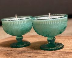 two green glass candles sitting on top of a wooden table