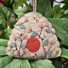 a felt ornament hanging from a tree with bees and flowers on it's side