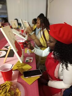 two women sitting at a table with paintings on it