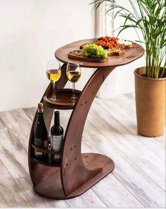 a wooden table with two wine glasses and some food on it next to a potted plant