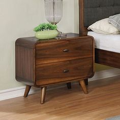 a nightstand with a plant on top of it in a bedroom next to a bed