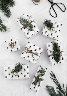 christmas presents wrapped in black and white paper with pine branches tied to them, surrounded by scissors