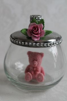 a pink teddy bear in a glass jar with a rose on it's top