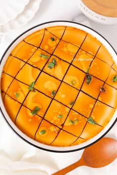 an orange dessert with green toppings in a white bowl next to a wooden spoon