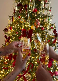 three people toasting champagne in front of a christmas tree with lights and decorations on it