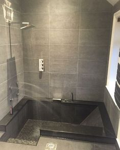 a bathroom with gray tiles and a black bathtub in the corner, next to a shower head