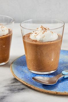 two glasses filled with chocolate pudding on top of a blue plate next to a spoon