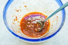 a blue and white bowl filled with sauce on top of a counter next to a spoon