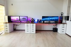 three computer monitors sitting on top of desks in front of a wall mounted tv