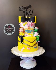 a yellow cake with characters on it sitting on top of a white pedestal in front of a black wall