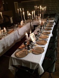 a long table is set with plates and silverware, lit by candlelight candles