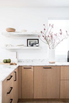 a kitchen with wooden cabinets and white marble counter tops, along with open shelving