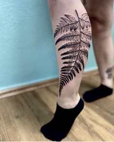 a woman's leg with a fern leaf tattoo on her left calf and black socks