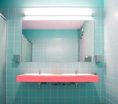 a bathroom with two sinks and a mirror in it's corner, against a blue tiled wall