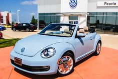 a light blue volkswagen convertible parked in front of a dealership with other cars behind it