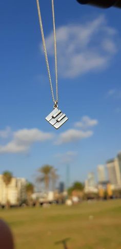 a small square pendant hangs from a silver chain in front of a blue sky with white clouds