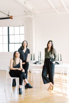 three women sitting on chairs in an empty room with white walls and wooden flooring