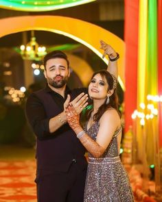 a man and woman standing next to each other in front of an arch with lights